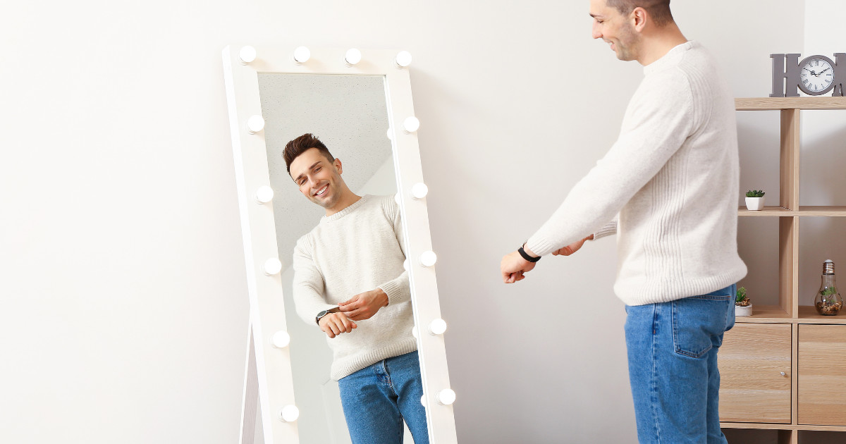 A man in a white t-shirt looks himself in the mirror.